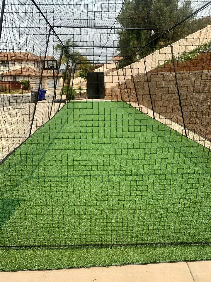 picture of a batting cage with artificial turf on the ground. Caged with clack mesh