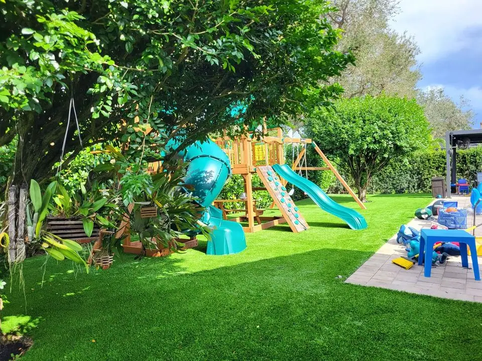 a backyard playground set up with two slides, swings and more, all safely set on artificial grass for playgrounds. Installed by Scottsdale Turf Pros