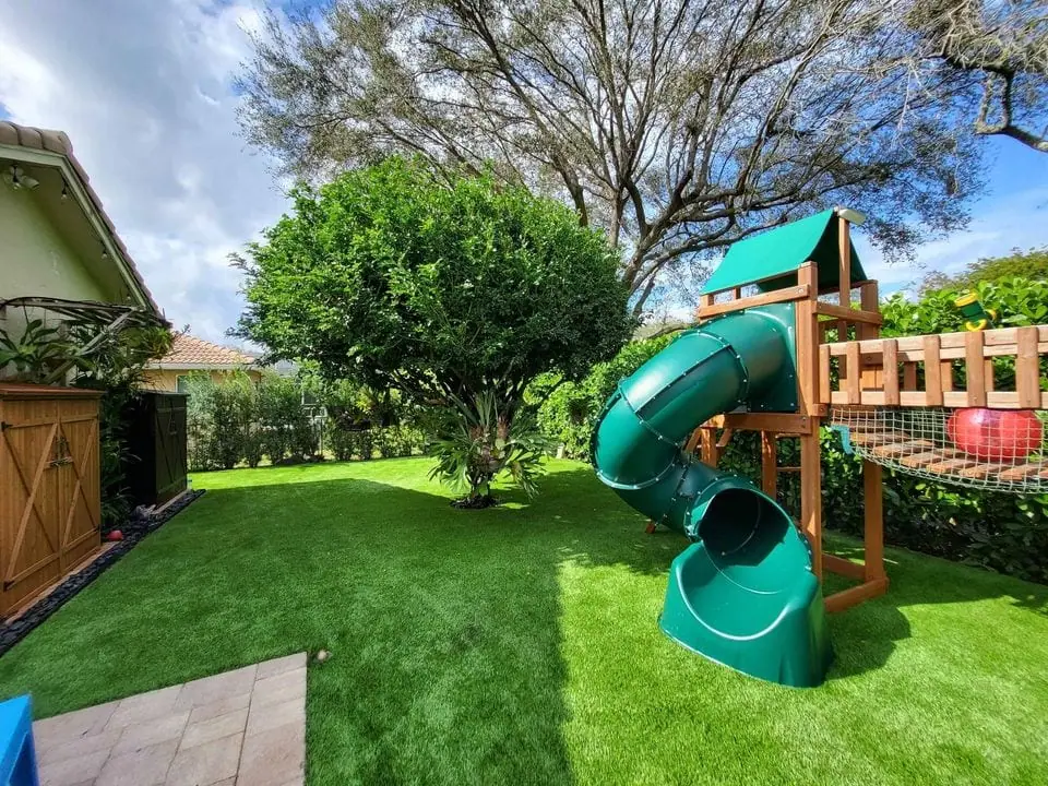 lush green artificial grass with a tree and platground with a slide and a swing bridge. Set in a backyard in scottsdale az